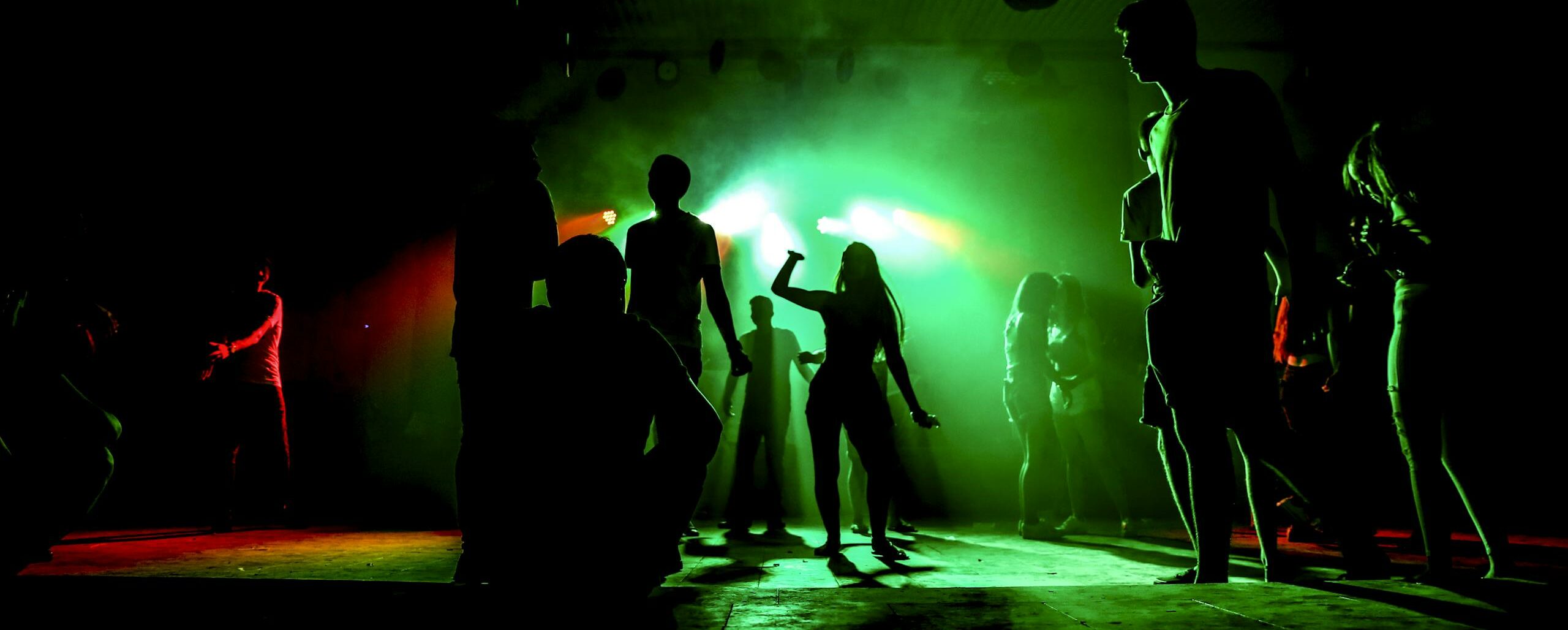 People dancing in a nightclub with colorful green lighting and vibrant atmosphere.