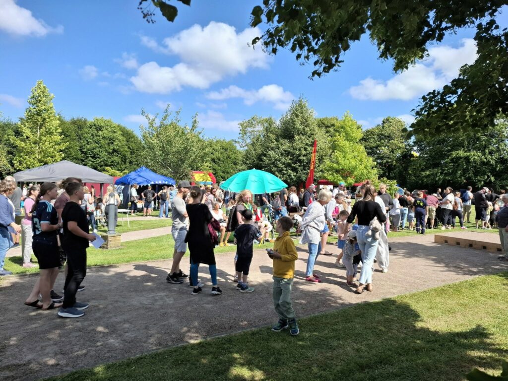 Besucherinnen und Besucher auf dem Spielefest 2026 in Hooksiel mit Marktständen, Pavillons und zahlreichen Familien unter blauem Himmel.