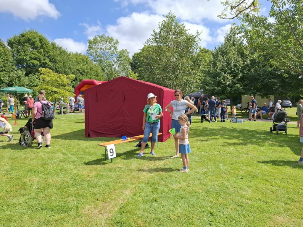 Ein Kind nimmt an einer Wurfspiel-Mitmachstation beim Spielefest 2026 in Hooksiel teil, während Familien und weitere Besucher das abwechslungsreiche Festprogramm im Park genießen.
