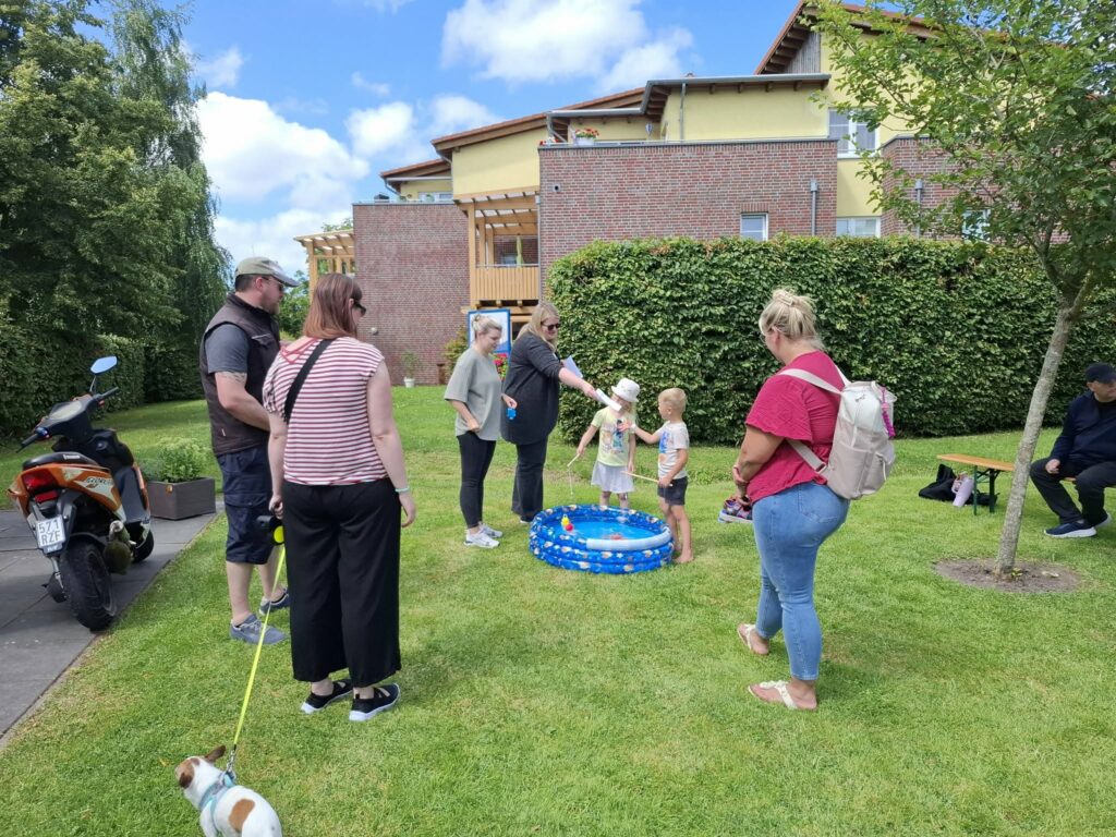 Kinder spielen beim Spielefest 2026 in Hooksiel an einer Angelspiel-Mitmachstation mit einem kleinen Wasserbecken, während Familien das Geschehen auf dem sonnigen Festgelände verfolgen.
