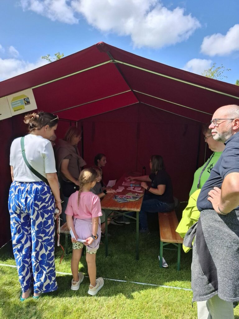 Kinder und Erwachsene nehmen an einem Wissens- und Mitmachangebot in einem Pavillon beim Spielefest 2026 in Hooksiel teil und informieren sich gemeinsam an einem Aktionsstand.