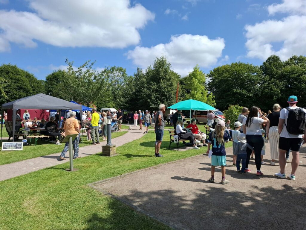 Besucherinnen und Besucher schlendern zwischen Pavillons und Mitmachstationen über das Spielefest 2026 in Hooksiel und genießen das vielfältige Familienprogramm im sonnigen Park.