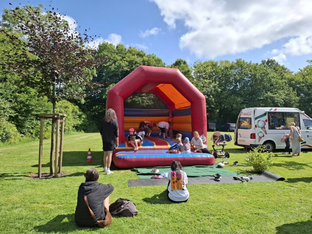 Kinder spielen auf einer Hüpfburg beim Spielefest 2026 in Hooksiel, während Familien auf der Wiese entspannen und ein Eiswagen am Rand des Festgeländes steht.