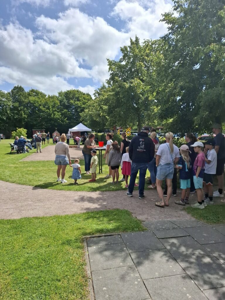 Besucherinnen und Besucher stehen beim Spielefest 2026 in Hooksiel an einer Mitmachstation im Park, während Familien und Kinder das Festgelände bei sonnigem Wetter genießen.