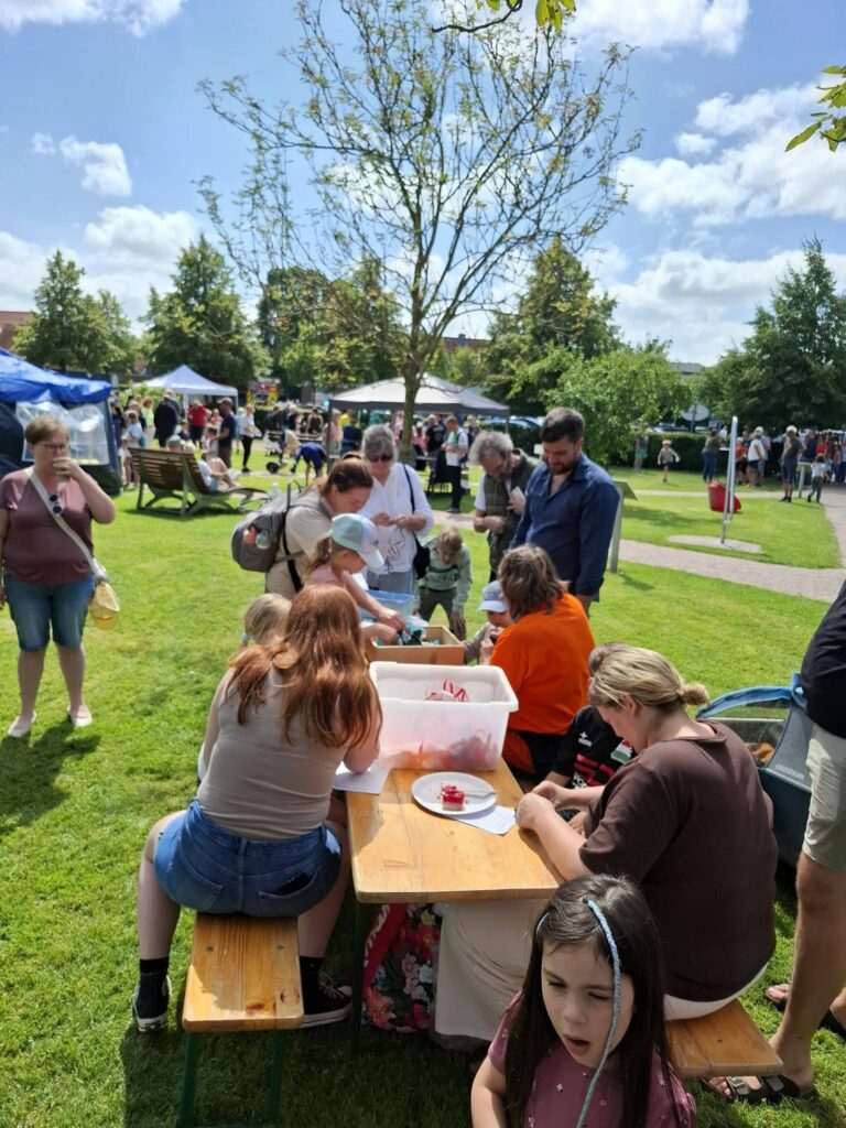 Kinder und Erwachsene basteln und gestalten gemeinsam an einem Mitmachstand beim Spielefest 2026 in Hooksiel, während zahlreiche Familien das Fest im Park besuchen.