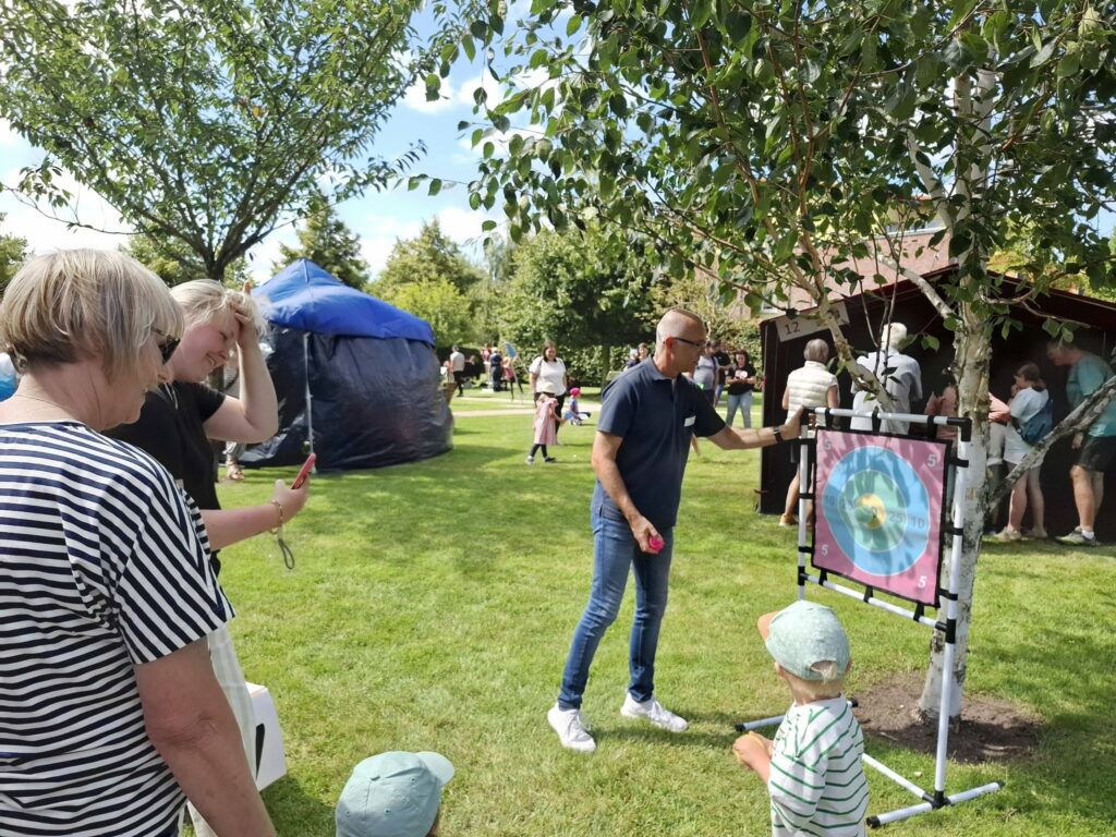 Ein Mann und ein Kind werfen bei einer Zielwurfstation Bälle auf eine Zielscheibe beim Spielefest 2026 in Hooksiel, während Familien die Mitmachaktion im Park verfolgen.